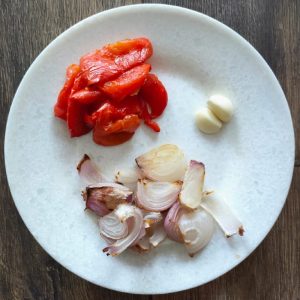 a plate with red bell pepper, garlic cloves and onions in it